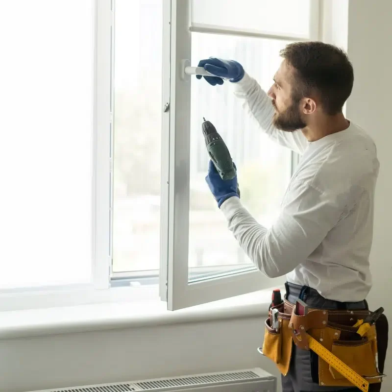 Un homme avec une ceinture à outils utilisant un tournevis et un tournevis électrique pour réparer une fenêtre.
