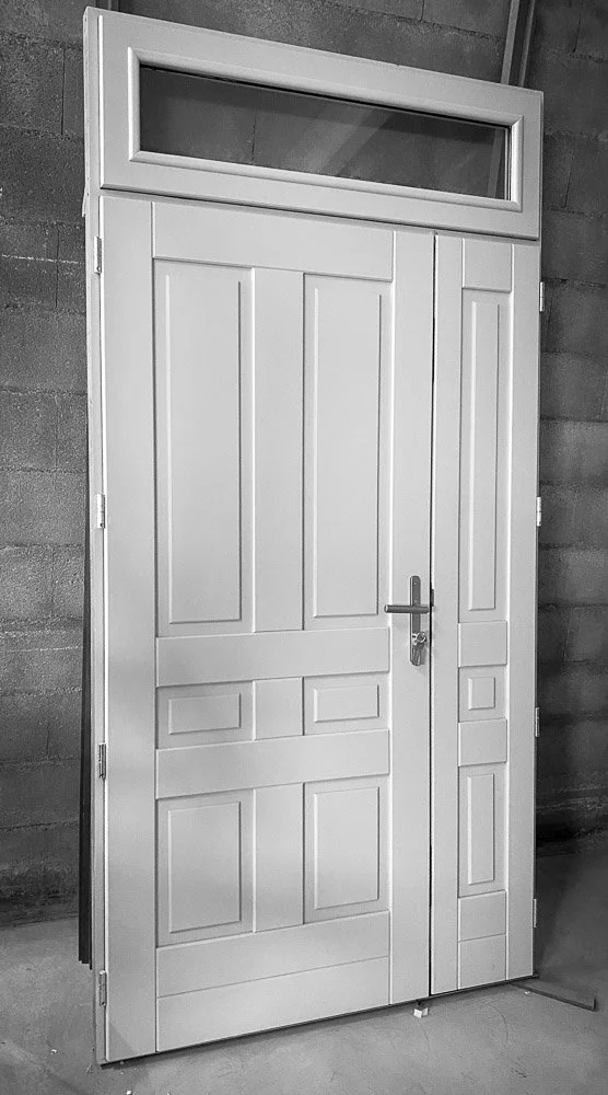 Une porte blanche en bois avec une fenêtre en haut : menuiserie fixée contre un mur en béton.