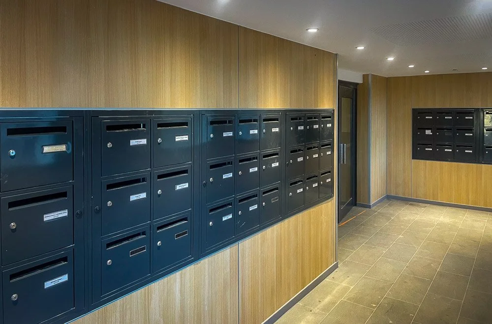 Fabrication et pose de boîtes aux lettres dans un hall d'immeuble toulousain avec murs en bois et sol en carrelage.