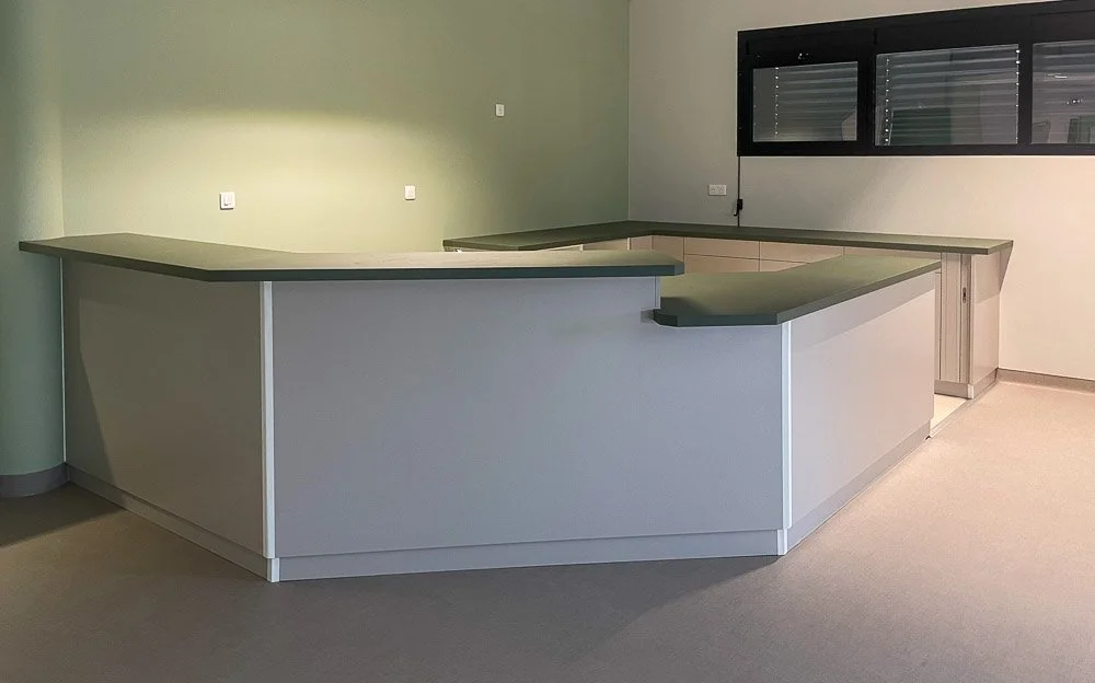 Un comptoir de réception fait avec une machine à commande numérique à Toulouse dans une pièce vide, avec une surface supérieure grise et un mur vert en arrière-plan.