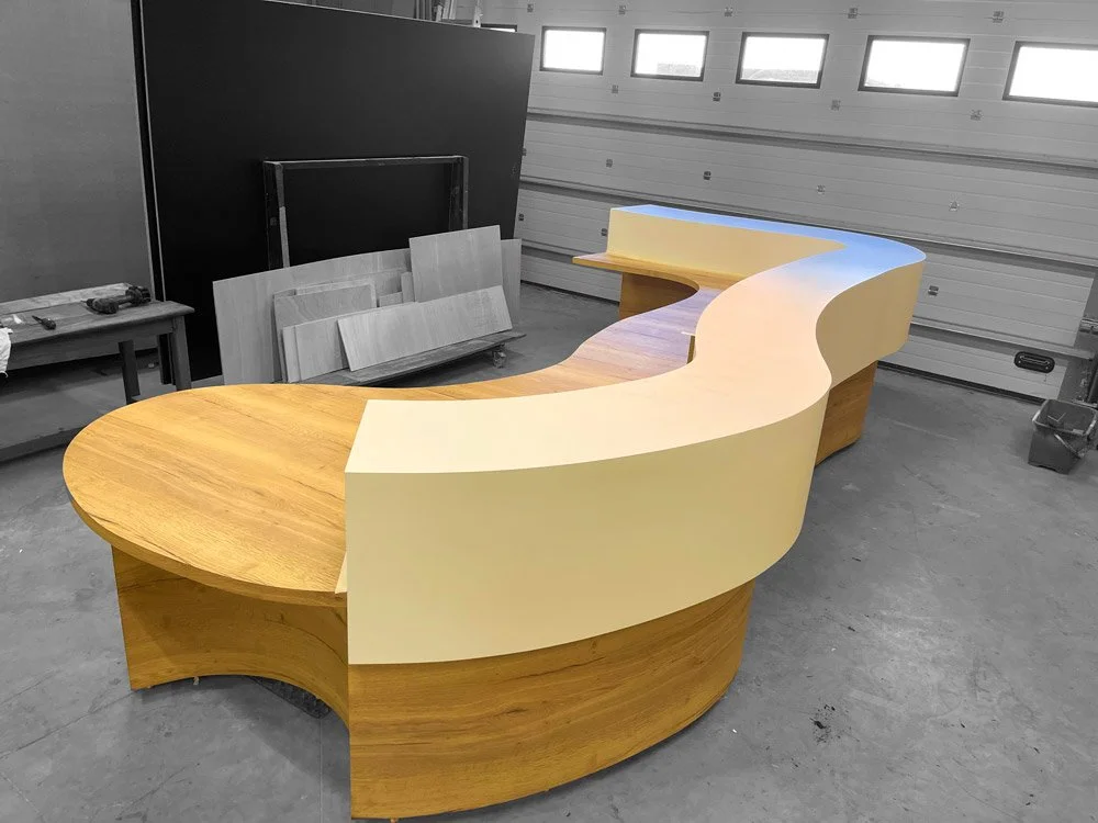 Un comptoir en bois courbé avec une surface blanche, dans l'atelier toulousain de Metrasud, en cours de fabrication