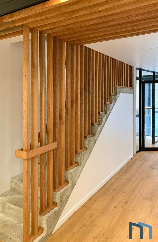 Escalier intérieur de menuisier avec rampes en bois et marches en béton, dans un espace moderne ouvert avec parquet en bois et grandes fenêtres en verre.