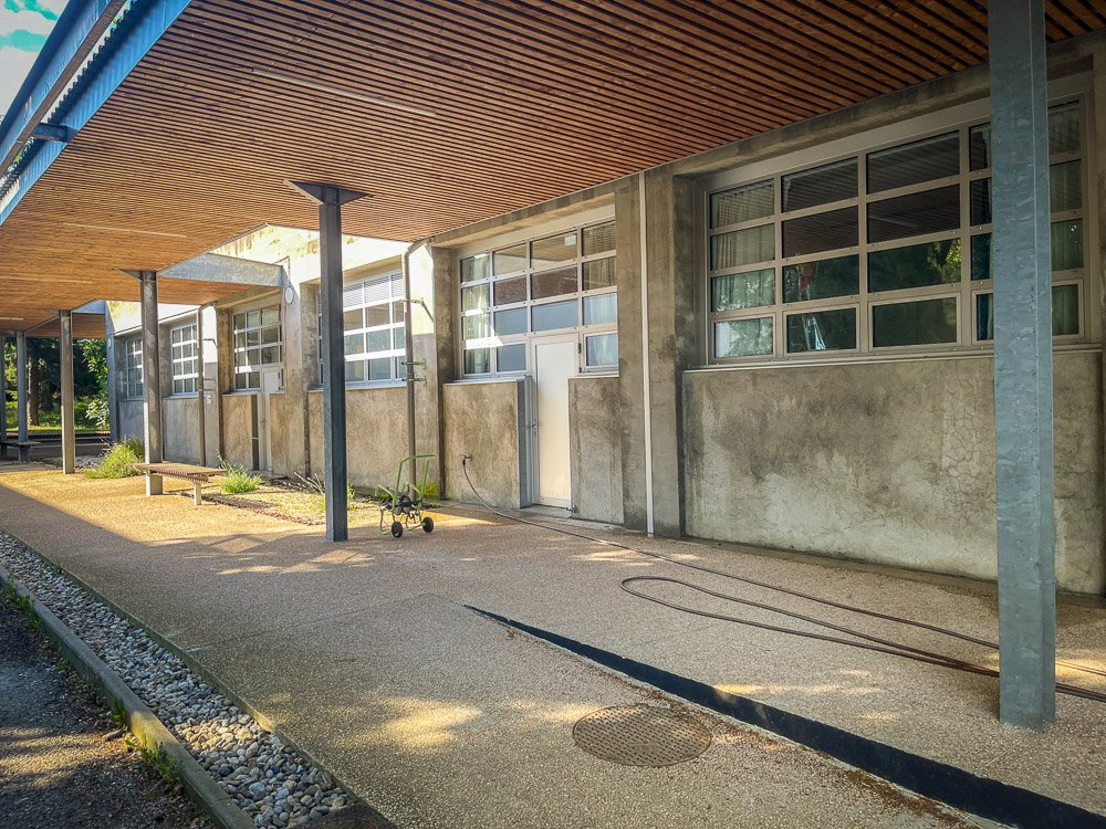 Façade d'un bâtiment moderne avec de grandes menuiseries en métal et  verre avec un auvent en bois soutenu par des colonnes en métal, trottoir devant.