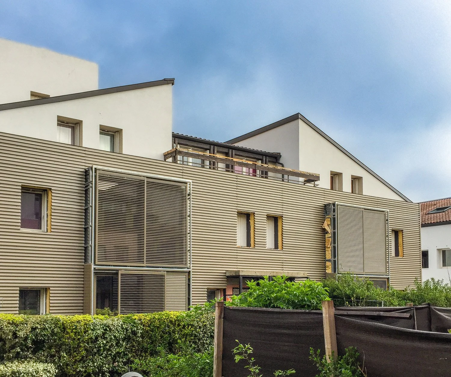 Réhabilitation d'un bâtiment résidentiel moderne toulousain avec fenêtres, volets en bois, et jardin en avant.