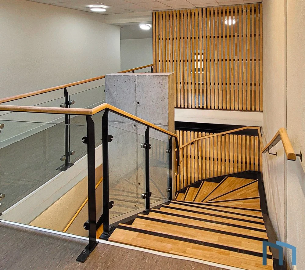 Escalier intérieur en colimaçon avec main courante en bois, murs en béton et panneaux en bois vertical.