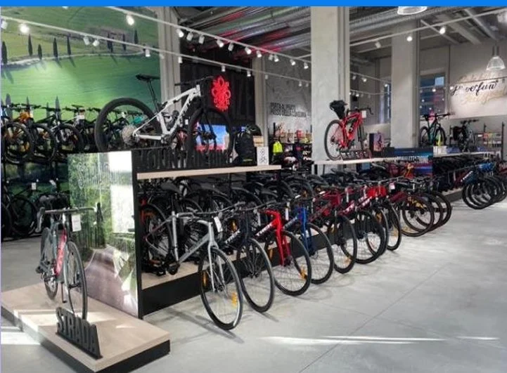 Indoor bike store with various bicycles displayed on racks and stands, including mountain, road, and electric bikes, in a well-lit modern setting.