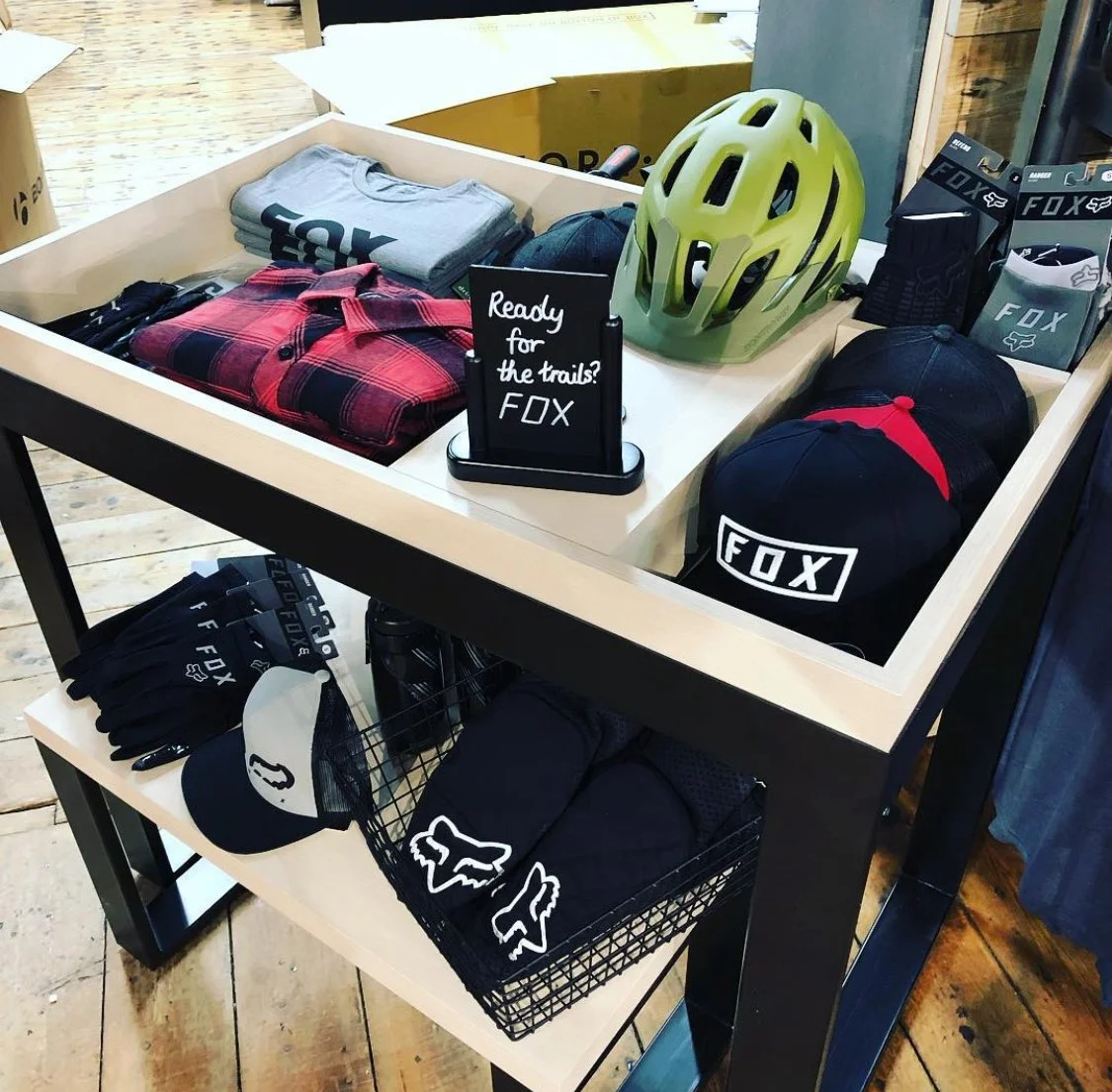 Display of biking gear including helmets, caps, gloves, and clothing with FOX branding on a retail table.