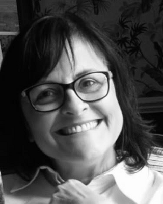 A woman with glasses smiling in a black and white photo.