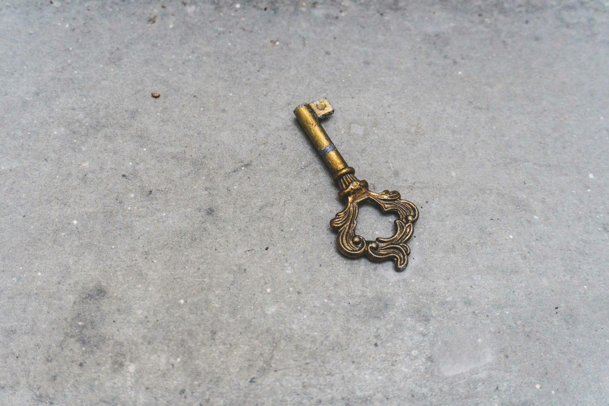 A vintage brass key with ornate detailing lying on a textured concrete surface.