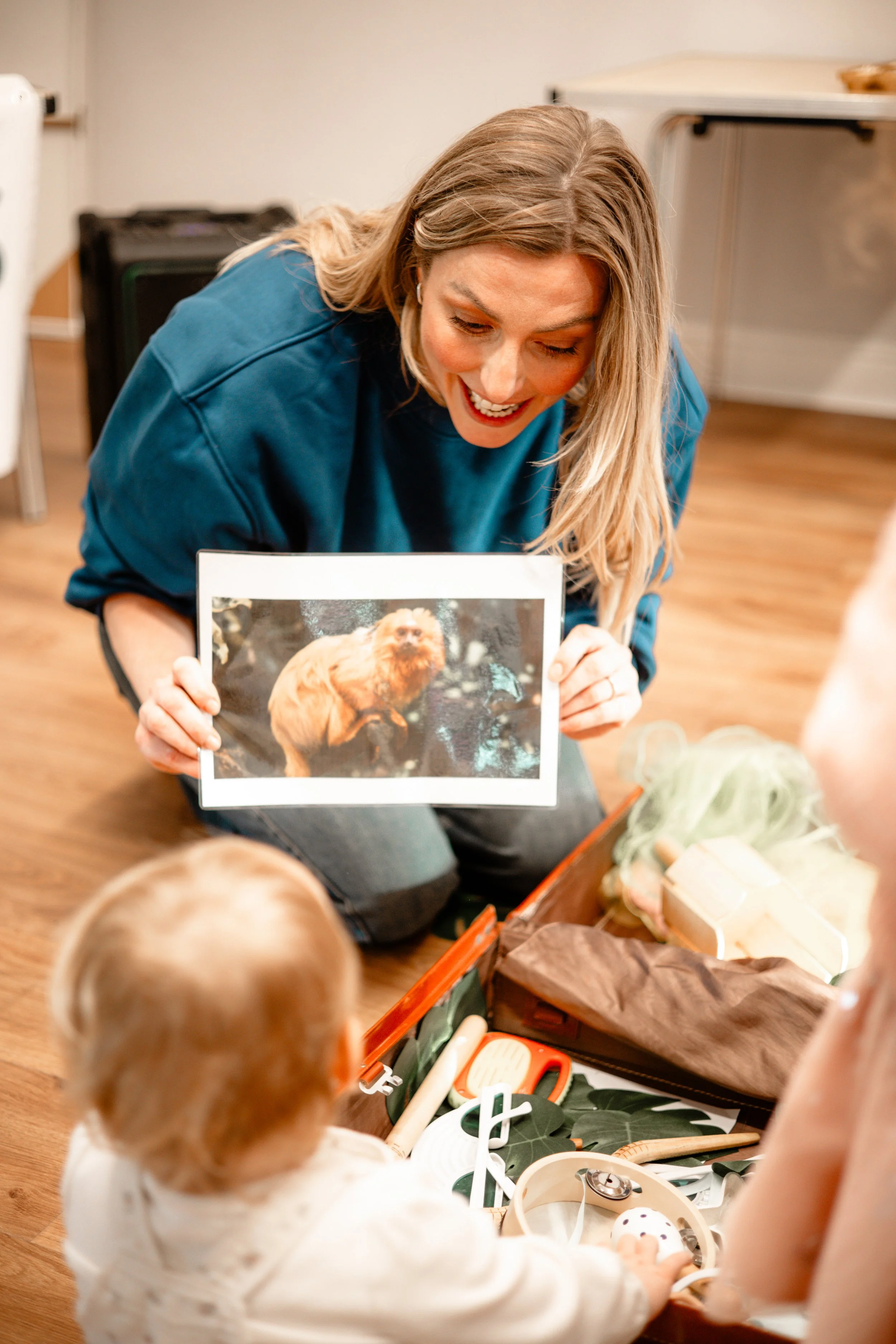 Woman showing a photo of a dog to children, sitting on the floor with a box of toys and supplies.