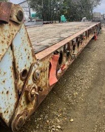 Rusty flatbed trailer with a worn wooden surface and damaged metal framework.