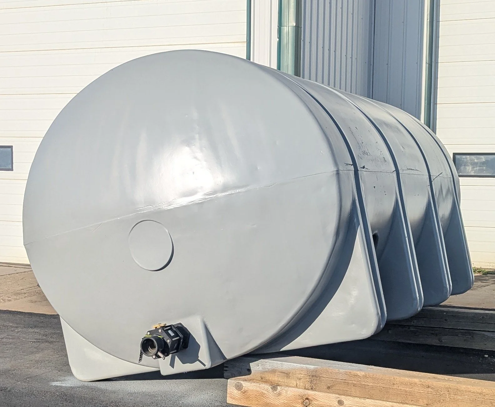 Three large, horizontal, metallic storage tanks placed outdoors on a paved surface next to a building with metal siding.
