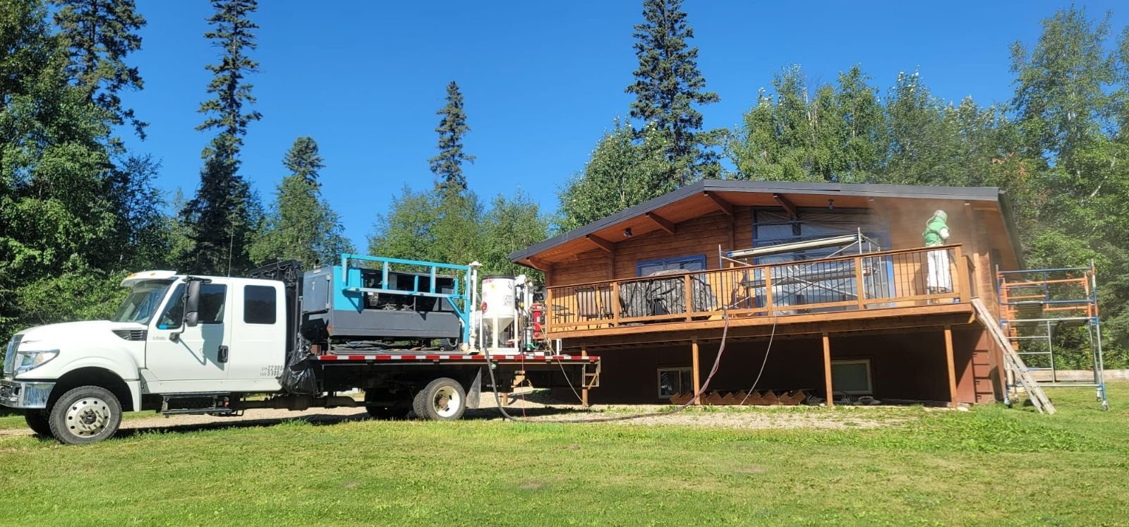 A clean white truck parked on a grassy lawn with a tall building in the background, surrounded by trees under a clear blue sky.