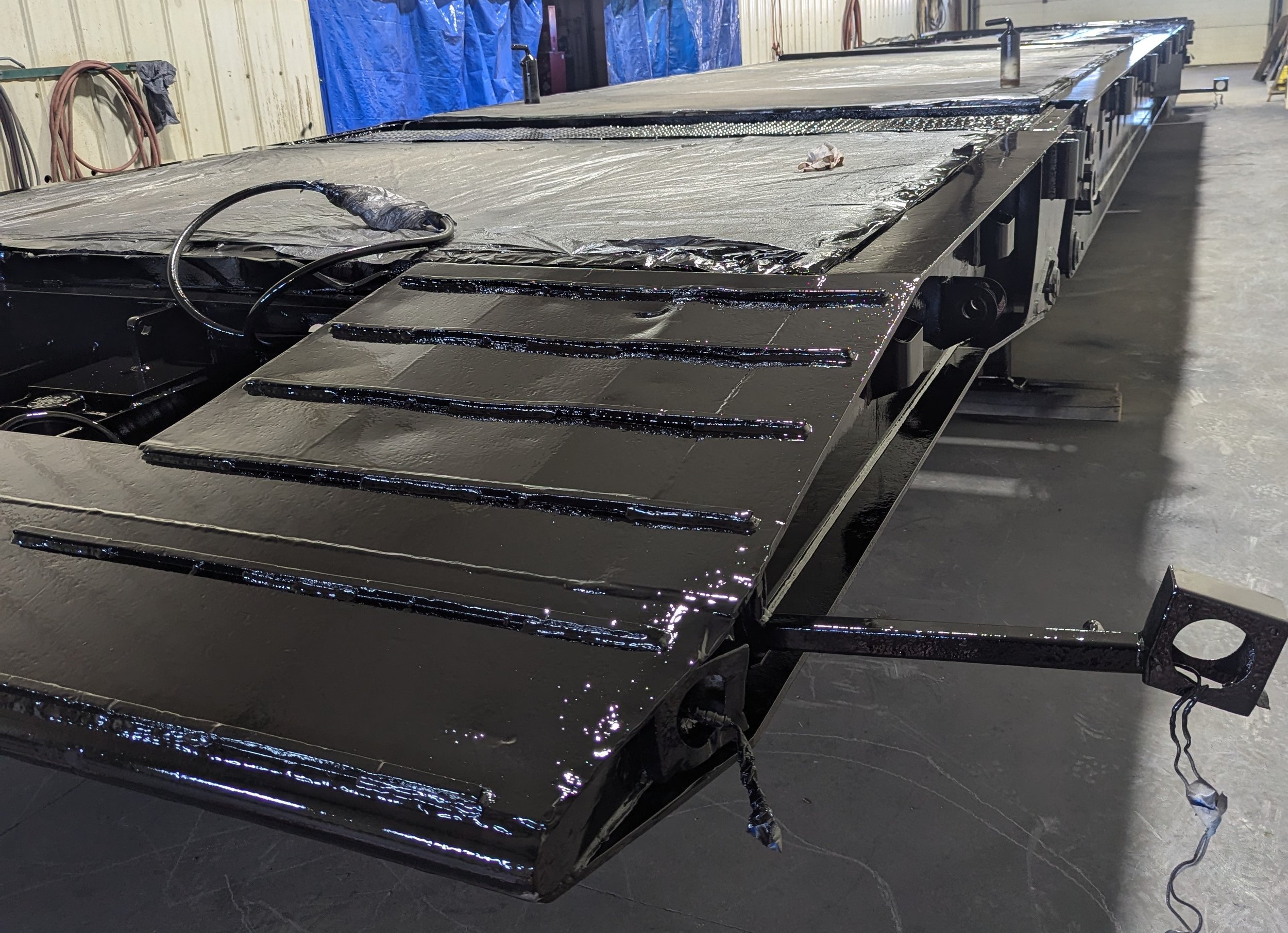 Black metal structure on workshop floor with shiny, freshly painted surfaces and some wiring, in a facility with blue tarps and tools in the background.