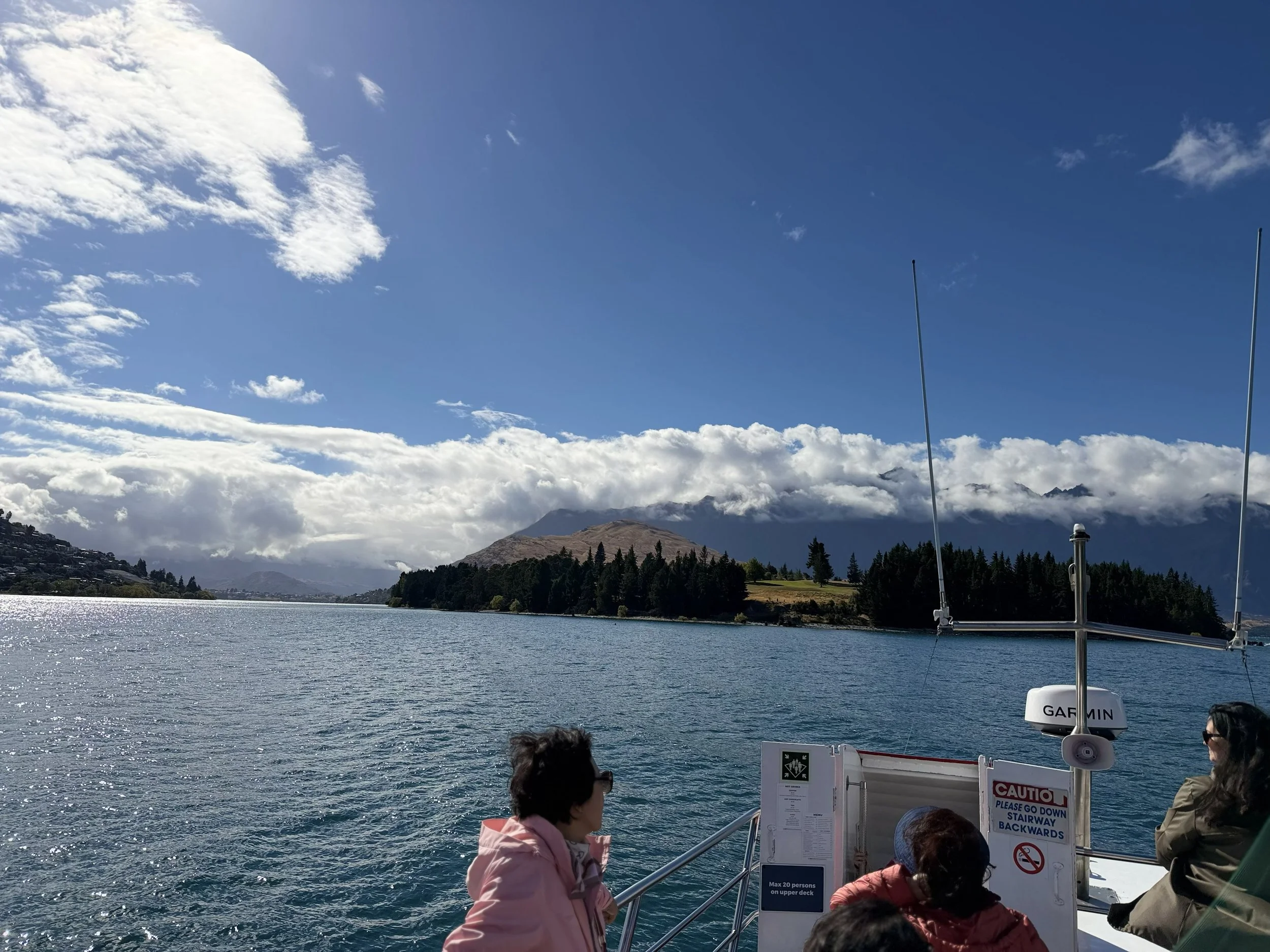 People on a boat viewing a body of water, with mountains and clouds in the background.