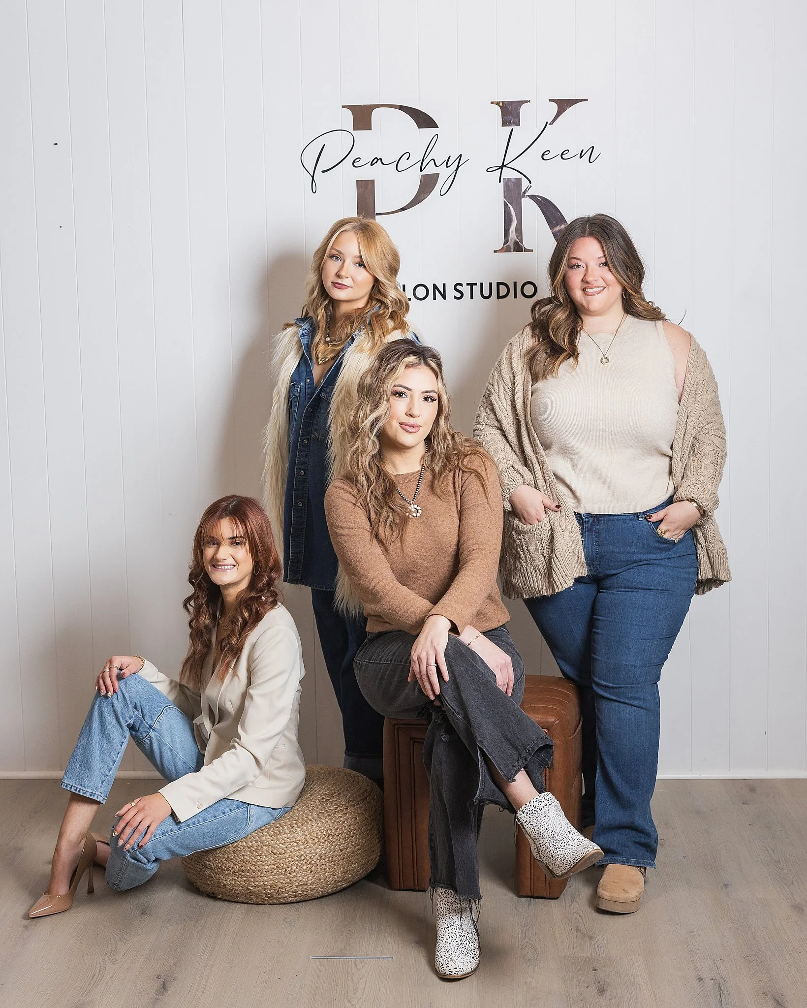 Five women posing in front of a wall that reads 'Peachy Keen Salon Studio' with some women sitting and some standing in stylish casual outfits.