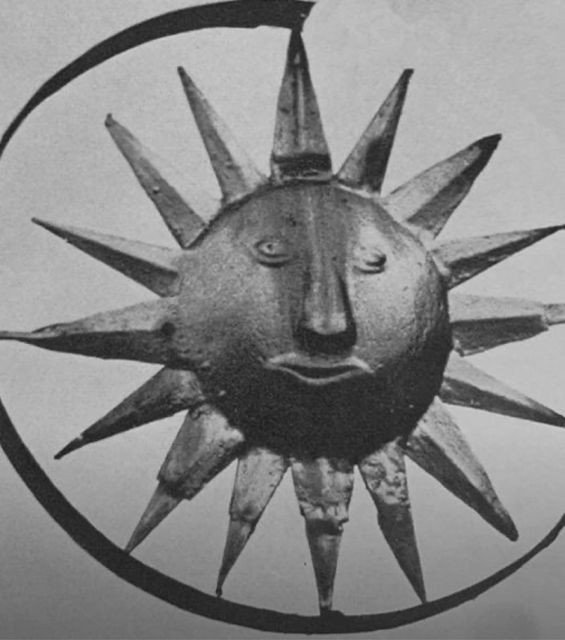 A sun sculpture with a human face, surrounded by rays, in black and white.