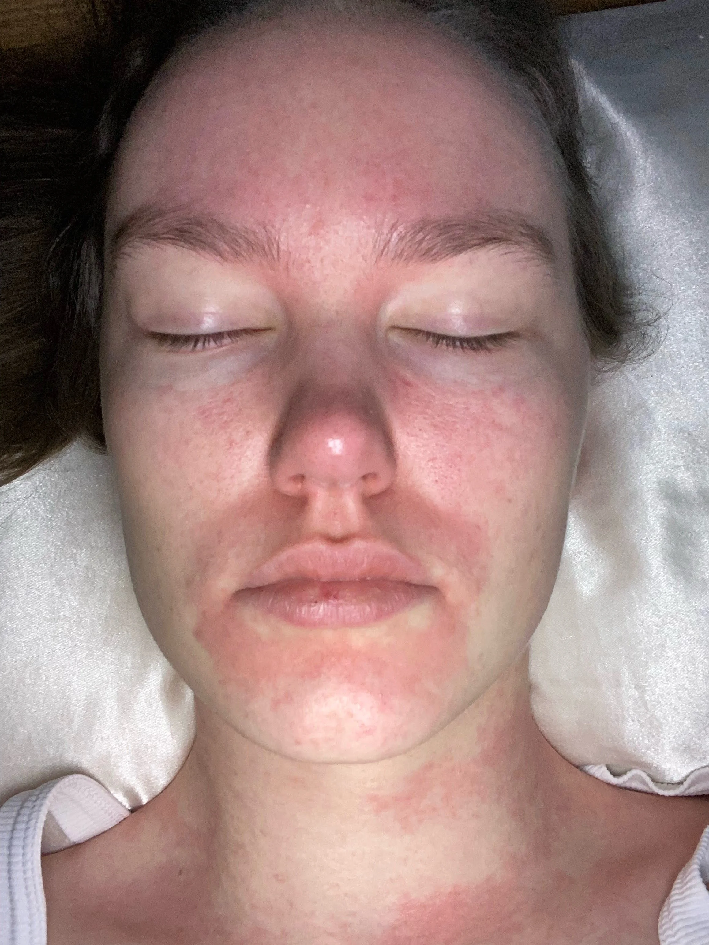 Lily Schubert, Sydney keynote speaker and content creator, lying down with eyes closed, appearing relaxed, with a white towel or cloth draped around the shoulders.
