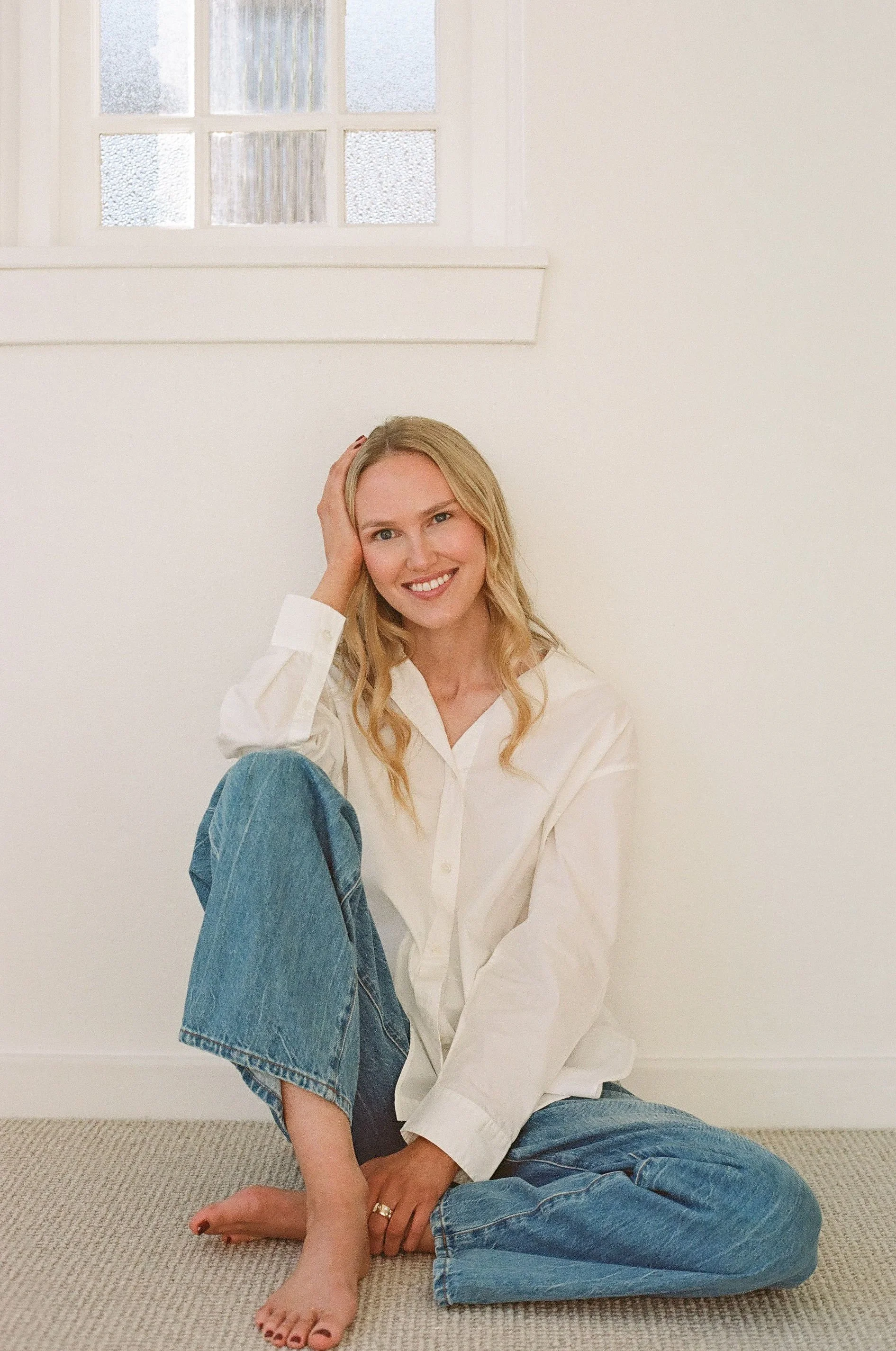 Lily Schubert, Sydney keynote speaker and content creator wearing a white button-up shirt and blue jeans, with her right hand resting on her head and her left arm resting on her knee.