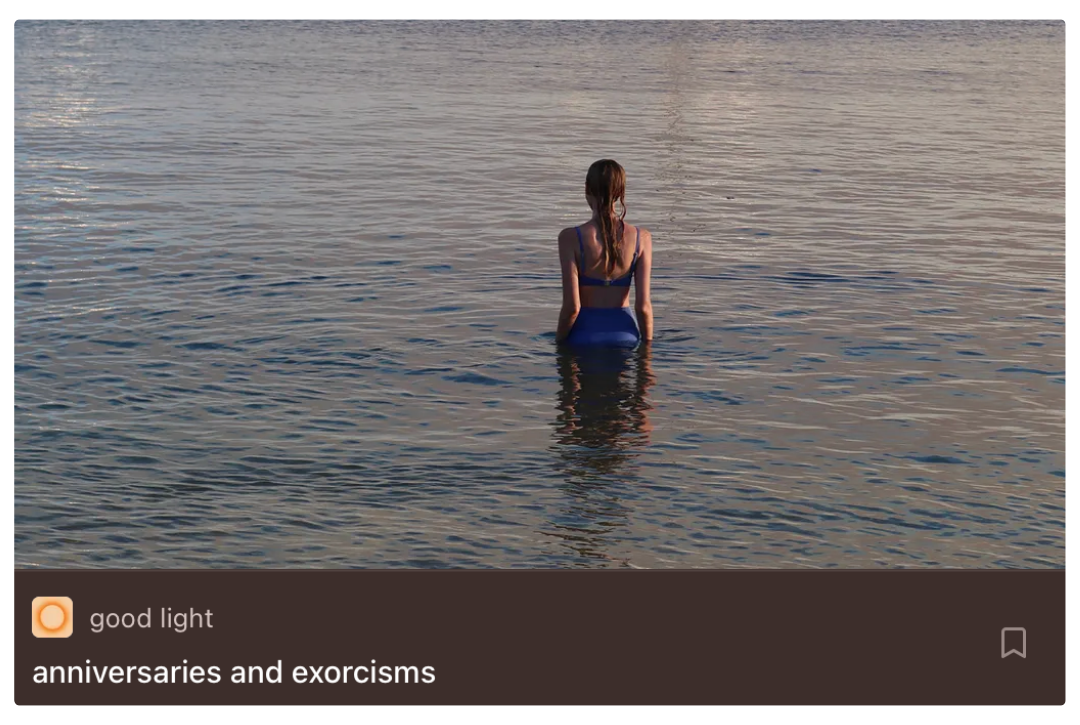 A woman in a swimsuit standing in calm water near sunset, with her back facing the camera.