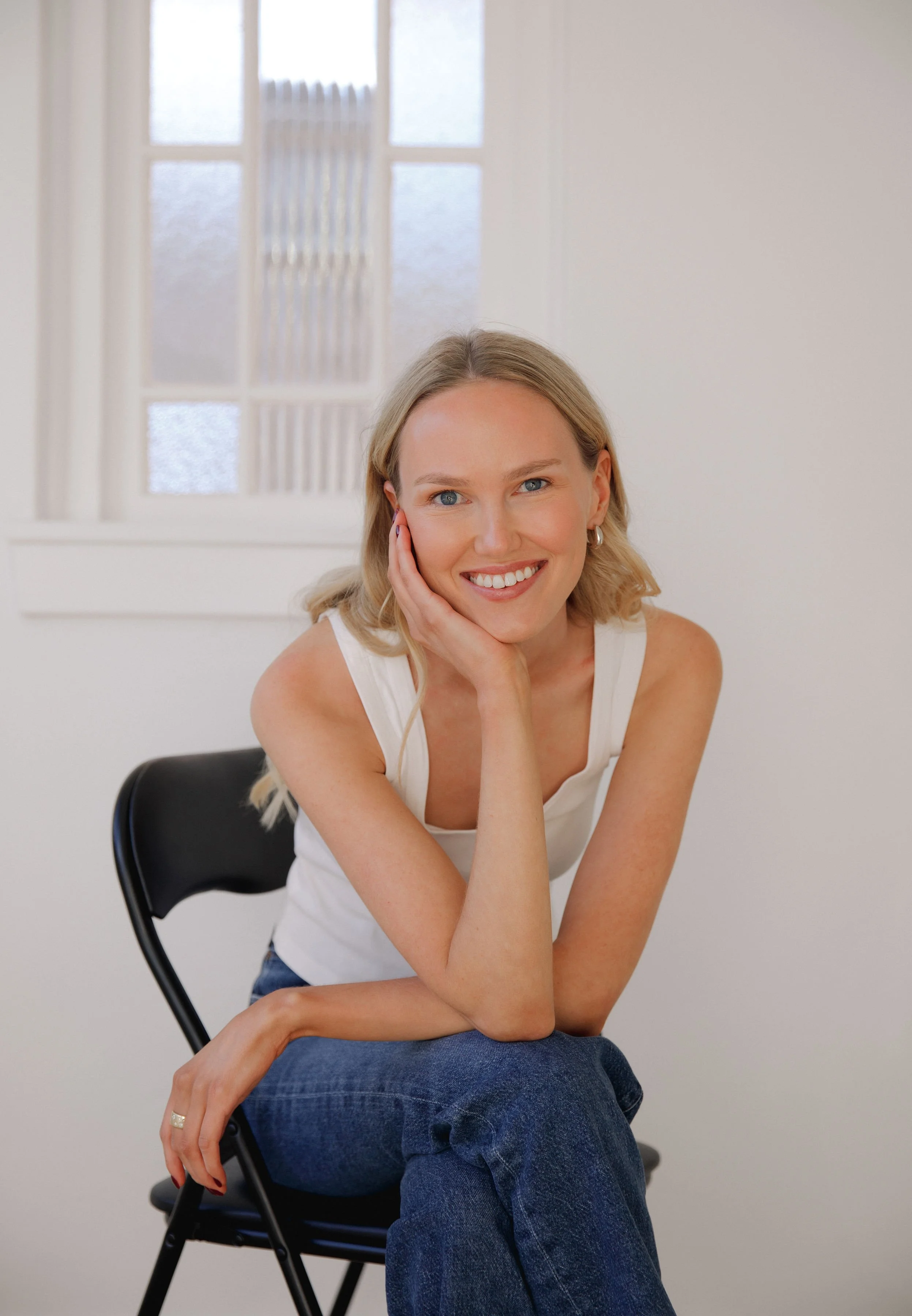 Lily Schubert, Sydney keynote speaker and content creator, sitting on a black chair in a white room with a window in the background.