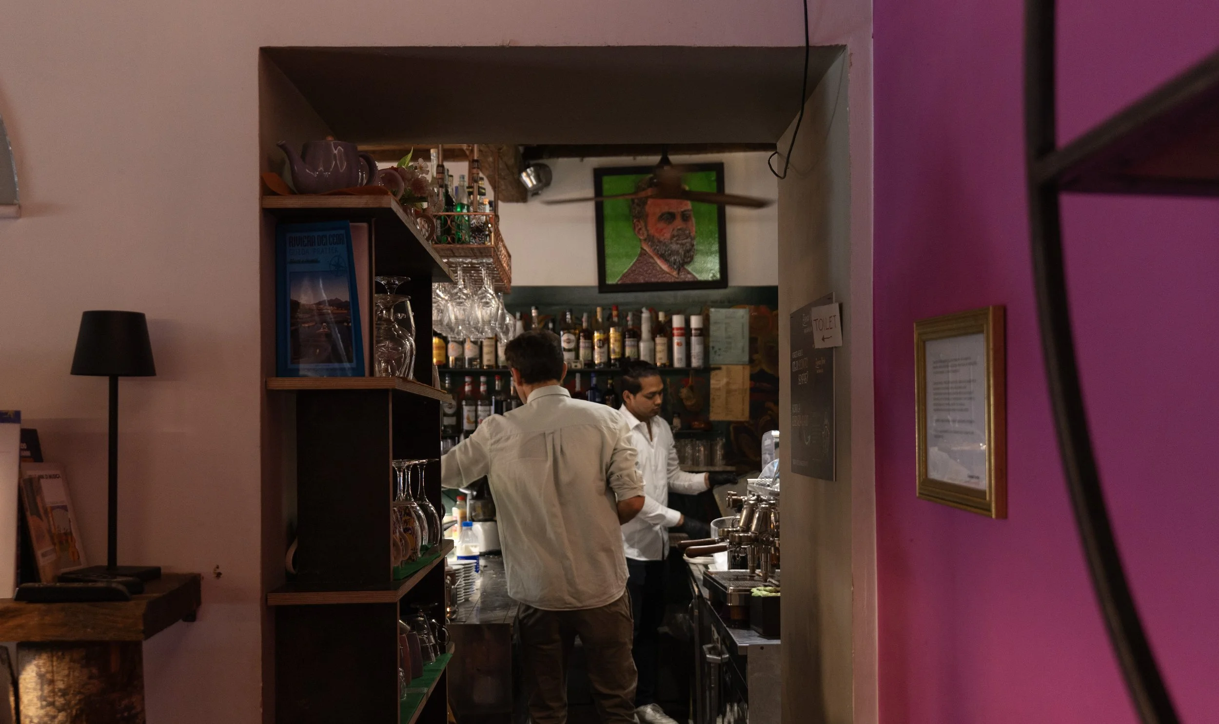 Interno di un bar con due baristi che preparano bevande e pareti colorate