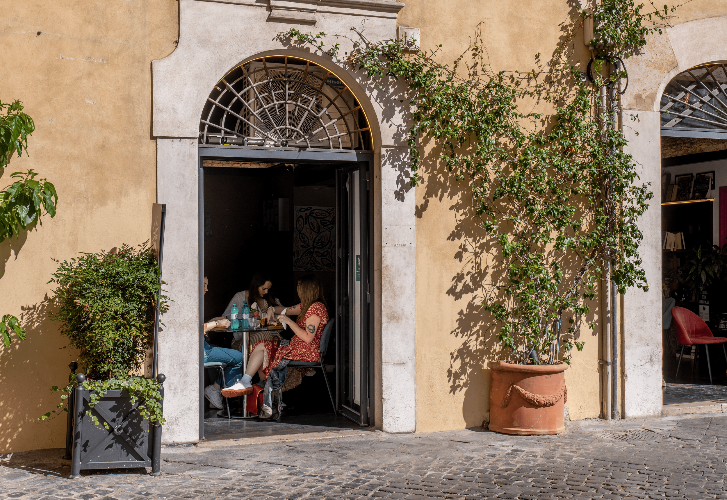 Persone che mangiano in un ristorante all'aperto in strada con pareti gialle e piante in vaso