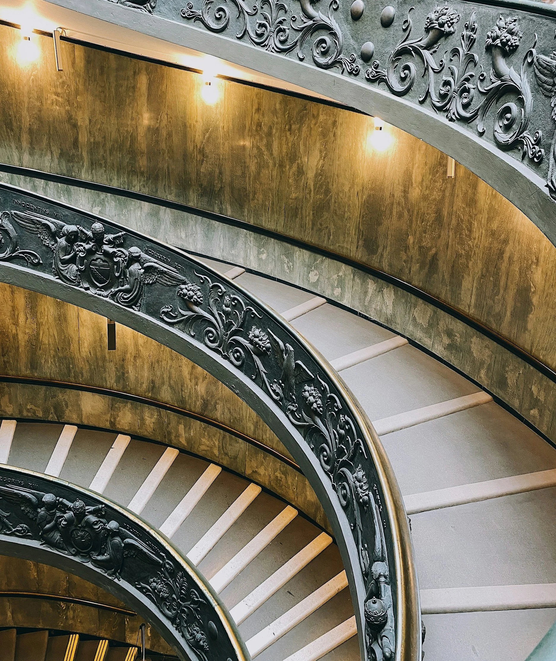 Spiraalvormige wenteltrap met sierlijke zwarte smeedijzeren leuningen en gouden muren, verlicht door zachte plafondverlichting.