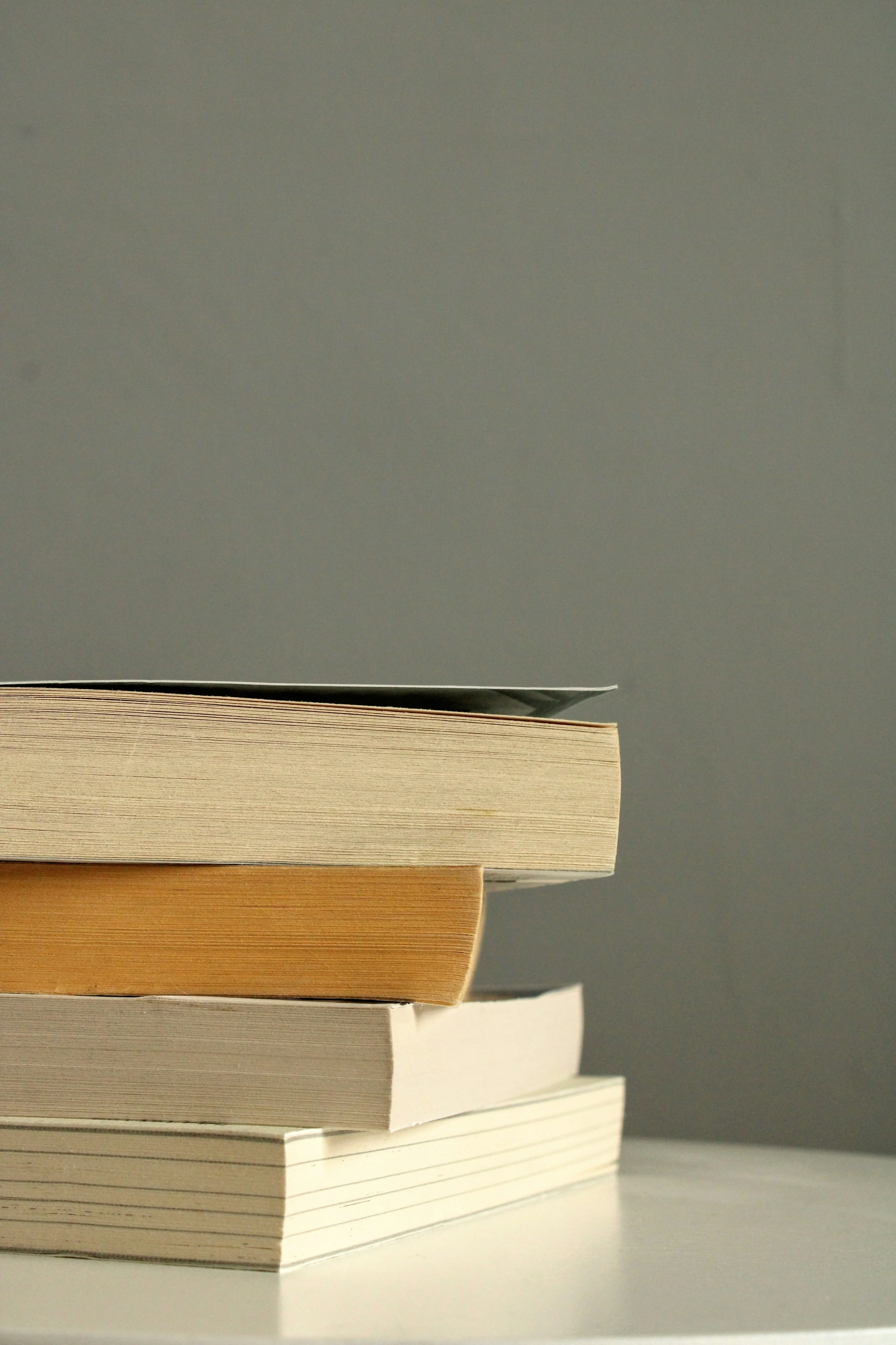 Stapel boeken op een witte tafel voor een grijze achtergrond.