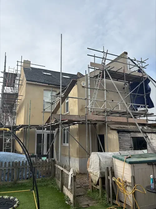 House under renovation with scaffolding around it, some parts of the house appear to be under construction or repair.