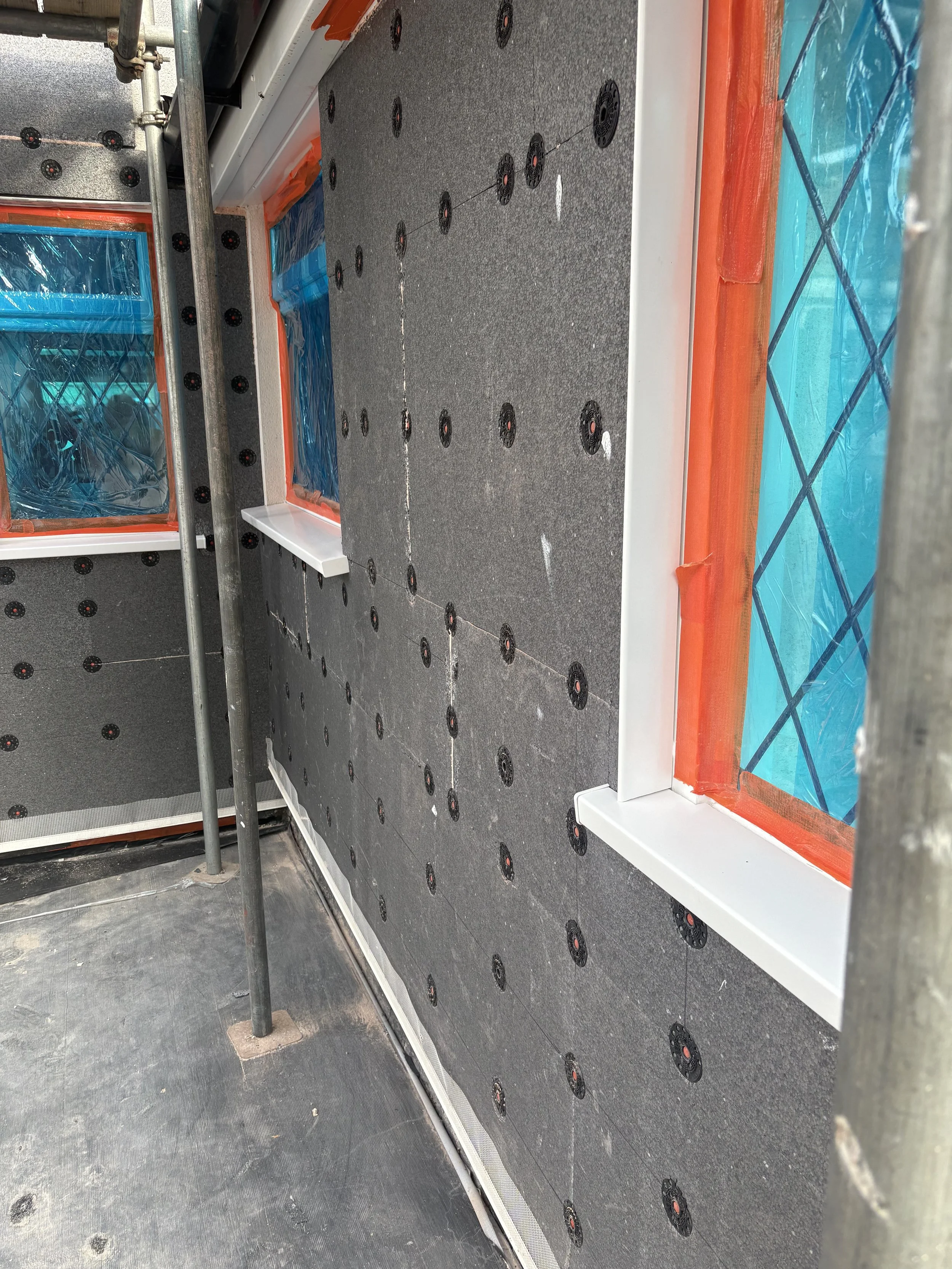 Interior of a building under construction with black insulation panels and blue plastic-covered windows.