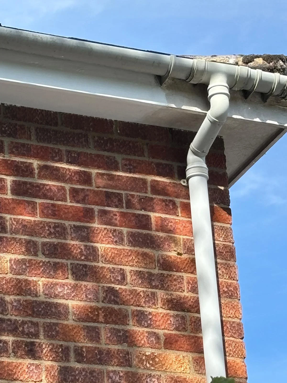 Close-up of a brick house corner showing a white gutter system with a downspout attached, under a blue sky.