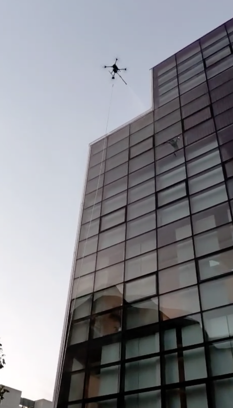 Ein Hubschrauber ist in der Luft über einem modernen glasverkleideten Gebäude und scheint Wartungsarbeiten durchzuführen.