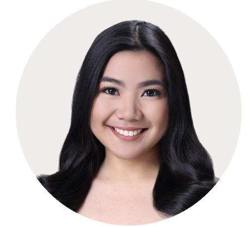 Close-up of a smiling young woman with long black hair and natural makeup, facing forward against a plain light background.