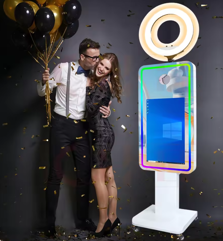 A man and woman celebrating with balloons and confetti, standing next to a digital kiosk with a glowing ring light.