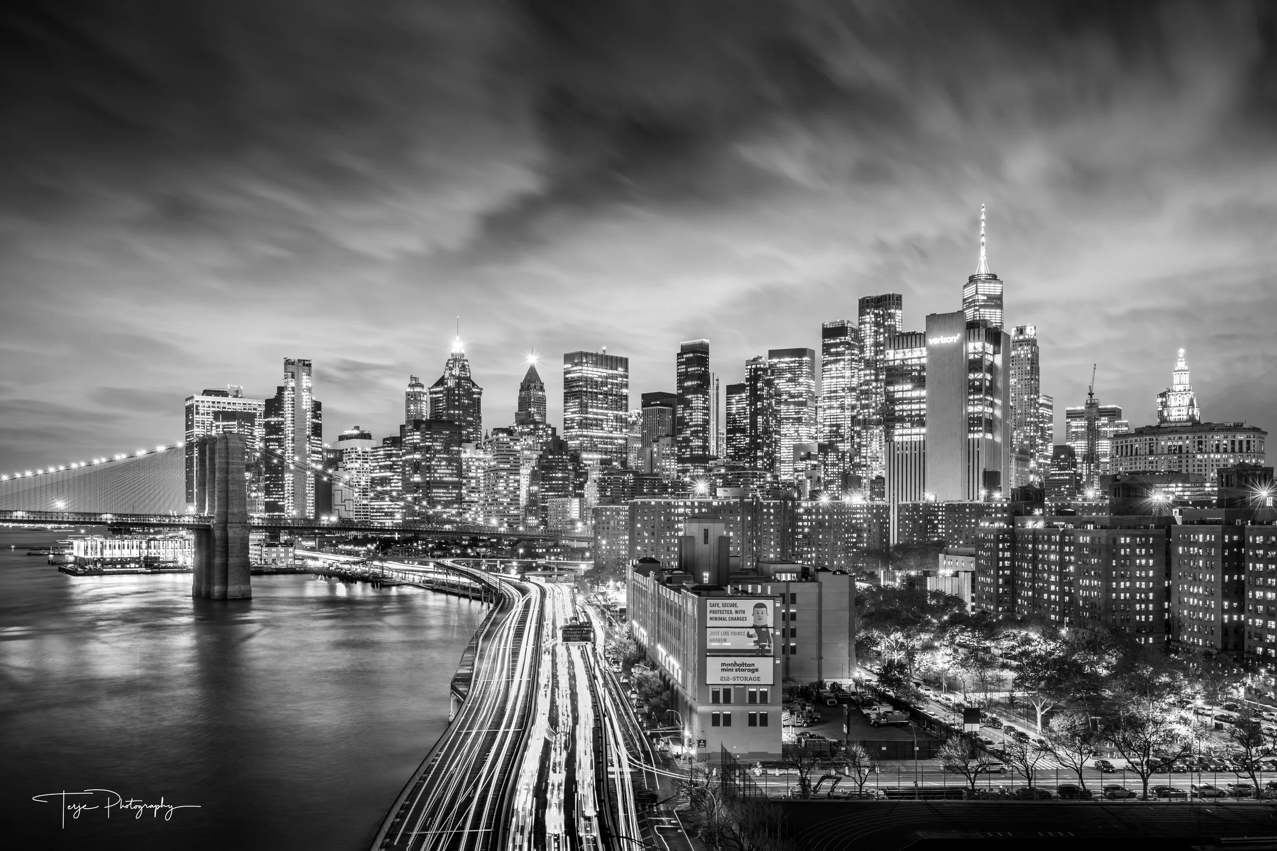 New York City skyline at night with long exposure light trails and dramatic clouds, black and white cityscape.