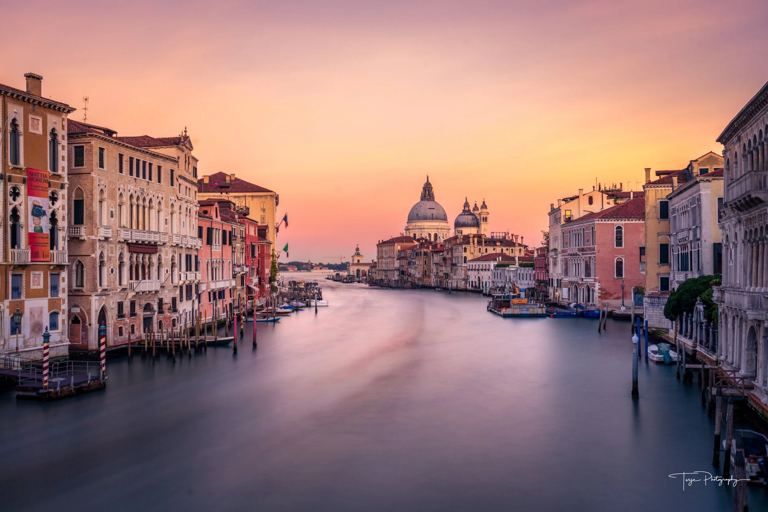 Venice canal at sunset from Accademia Bridge, warm sky and city lights, long exposure cityscape.