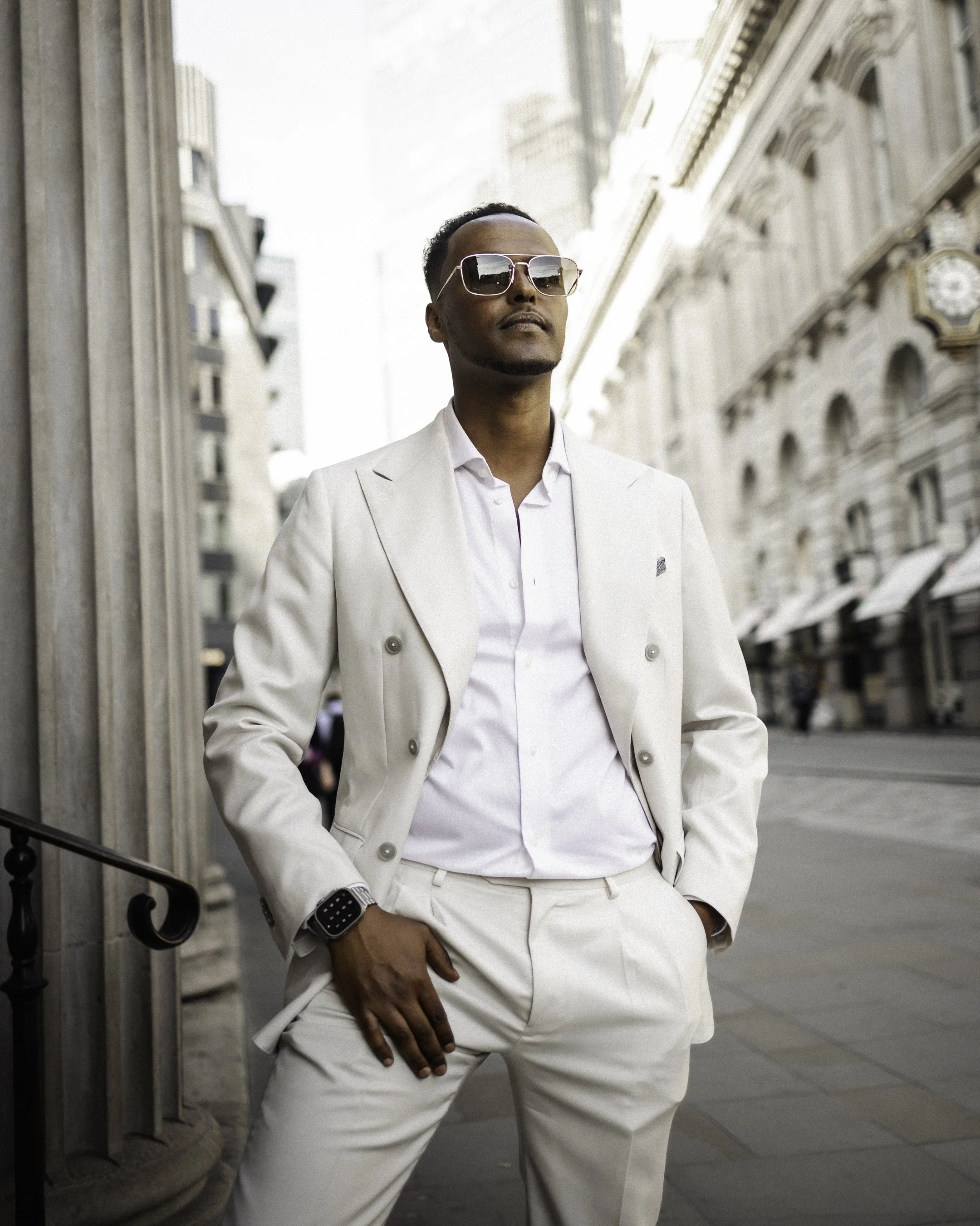A man in an all-white suit with sunglasses standing on a city street.