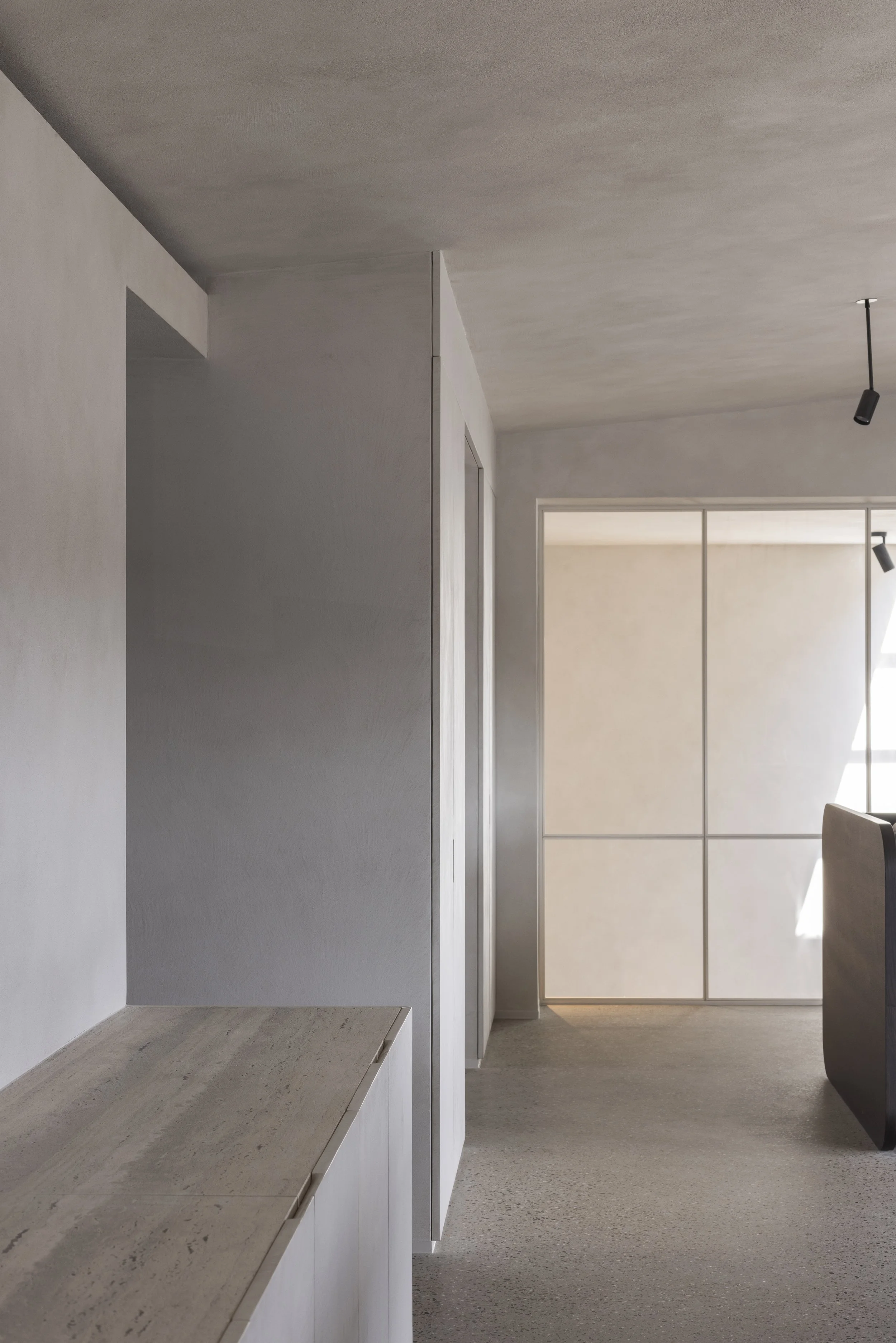 Interieur van een modern, minimalistisch huis met witte en grijze muren, een natuurlijke houten kast en een ruimte met grote ramen die veel natuurlijk licht binnenlaten.