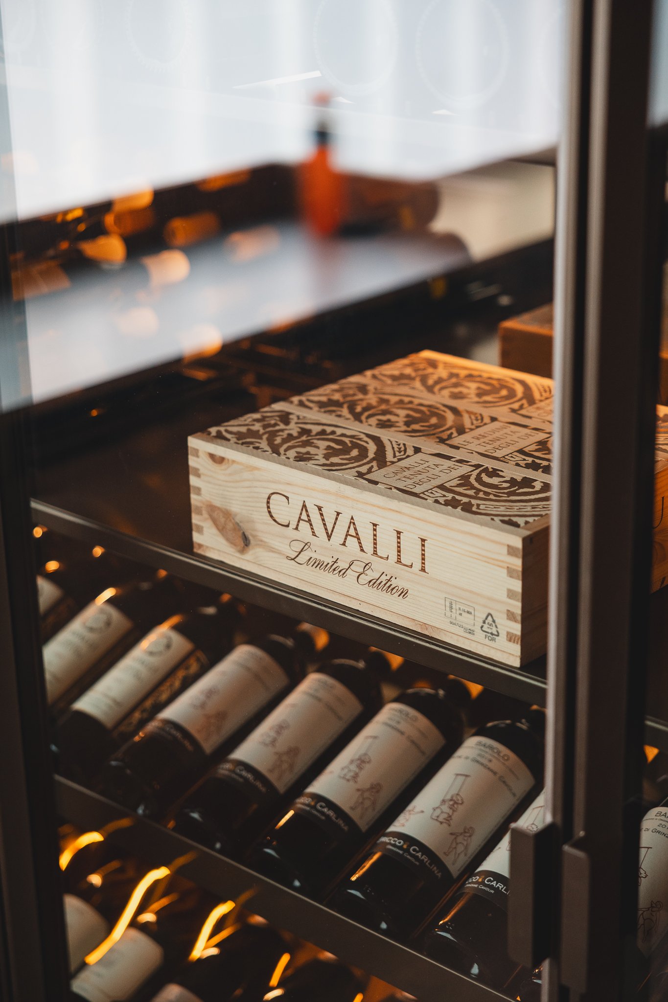 Een wijnkoelkast met wijnflessen en een houten wijnbox met de tekst 'CAVALLI Limited Edition'