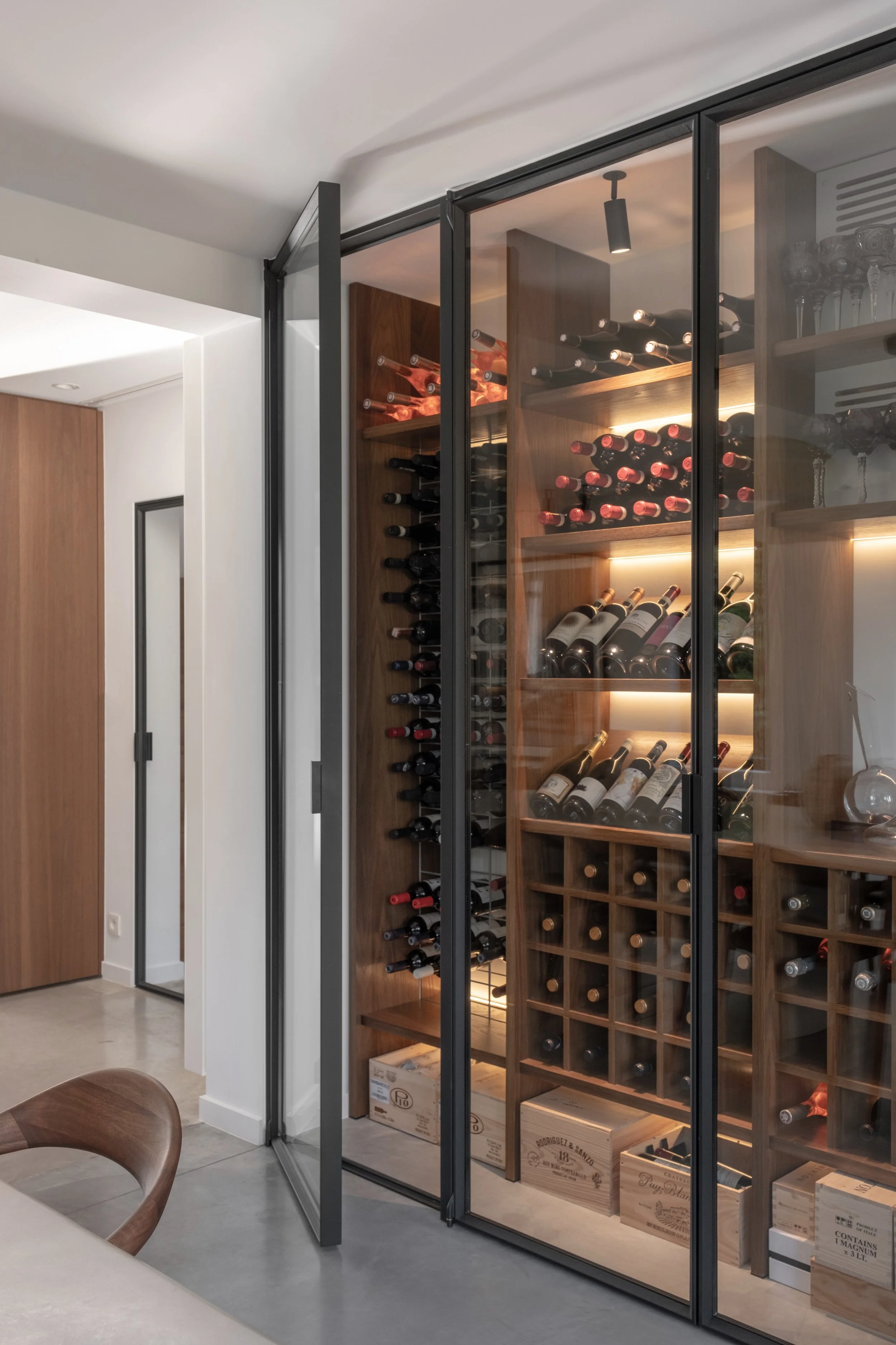 Wijnkast met wijnflessen en wijnkisten in een huis, zichtbaar achter glazen deuren.