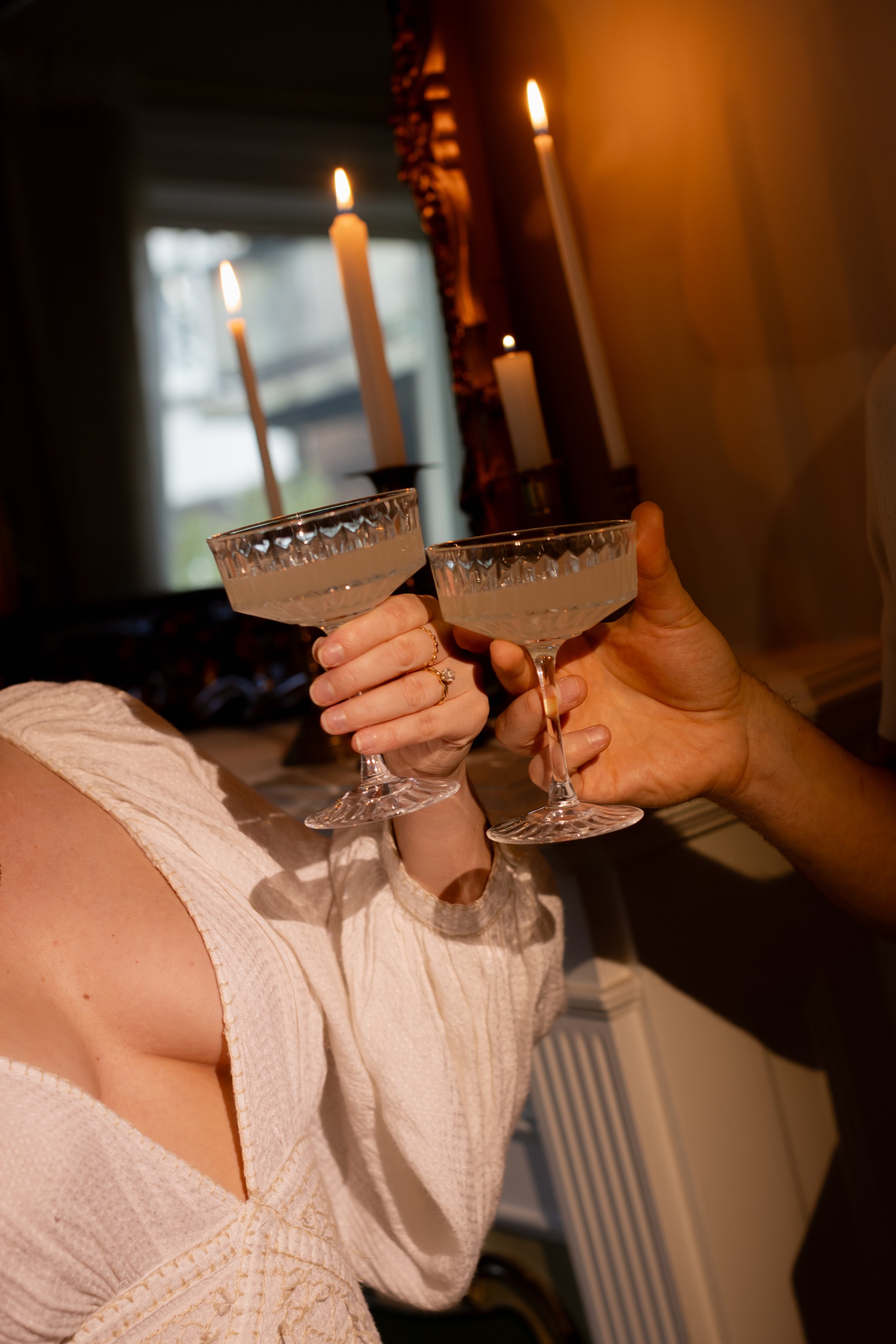 Two women toasting with champagne glasses in a warmly lit room decorated with candles.