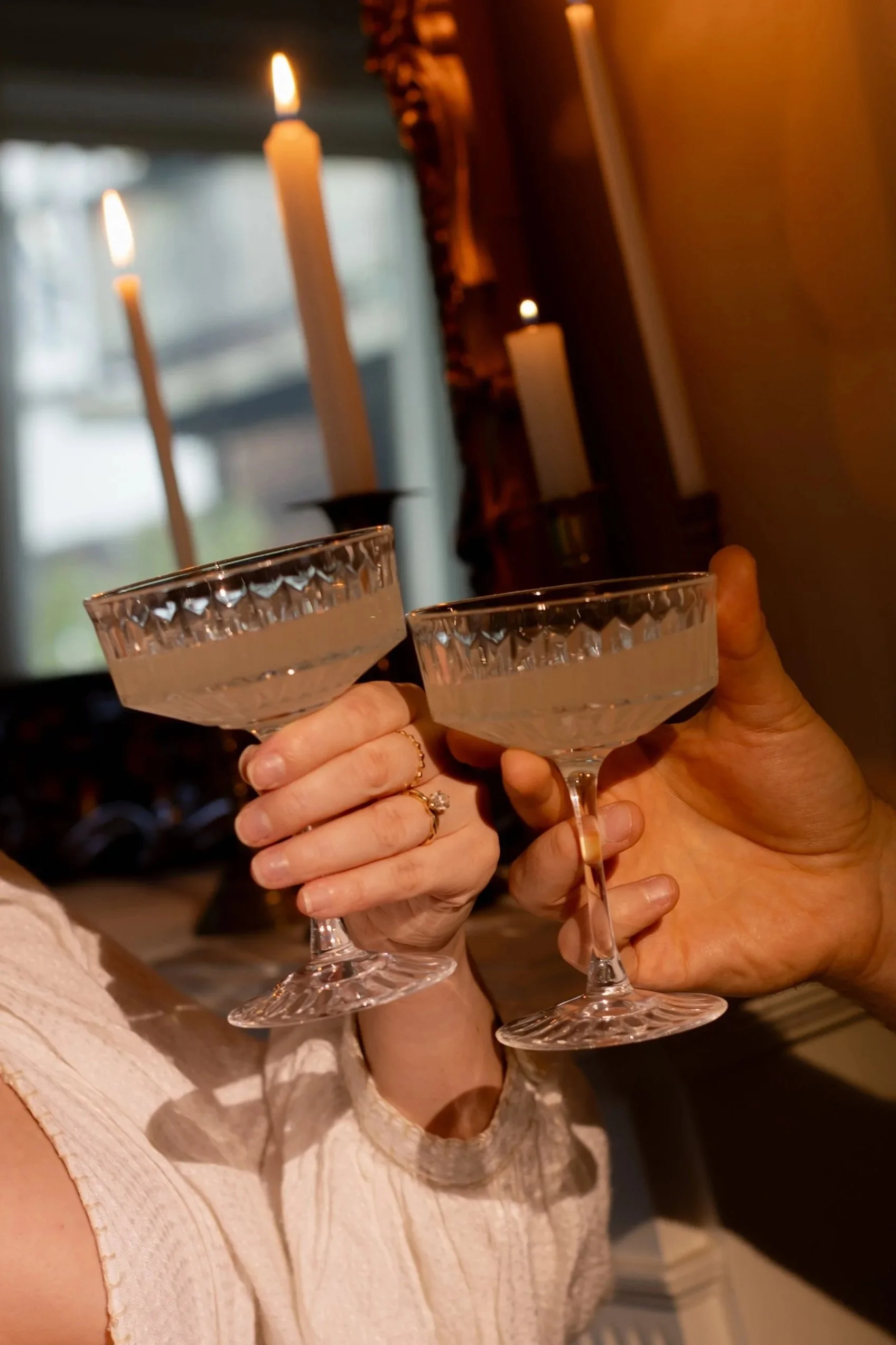 Two people clinking champagne glasses in a dimly lit room with candles in the background.