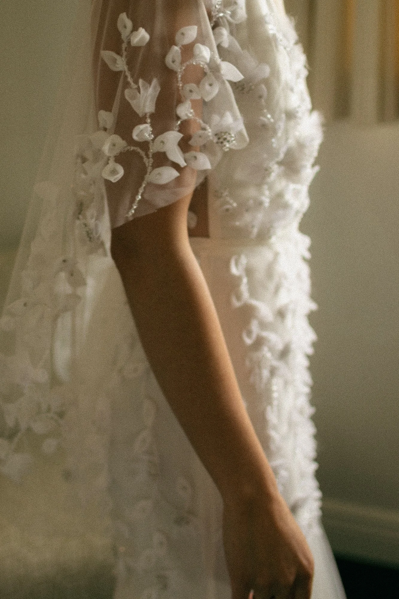 Close-up of a hand resting on a white, lace dress with floral embroidery, possibly a wedding dress.