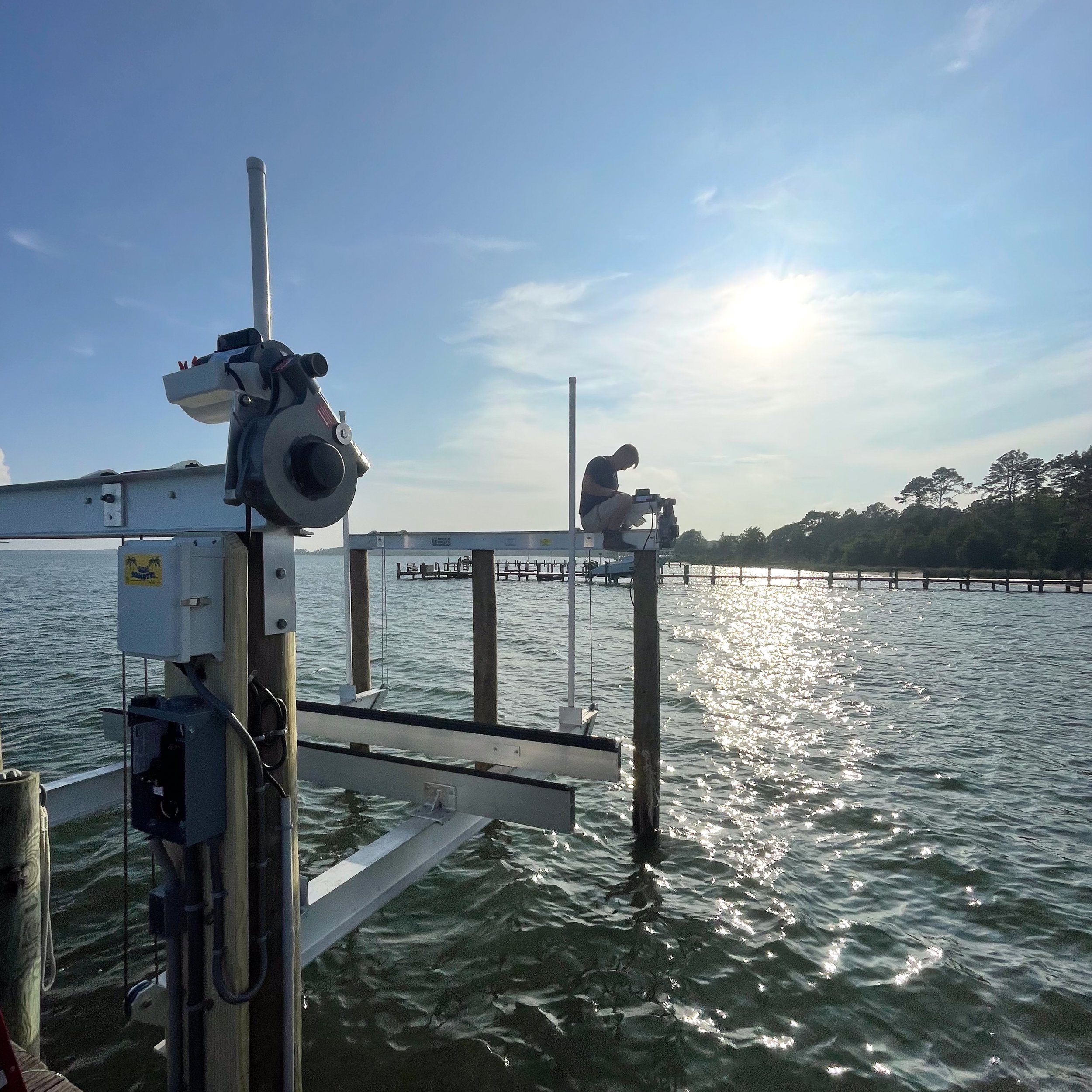 A Keeners Electric employee working on top of a dock piling with the sun low in the sky, and the water reflecting sunlight.