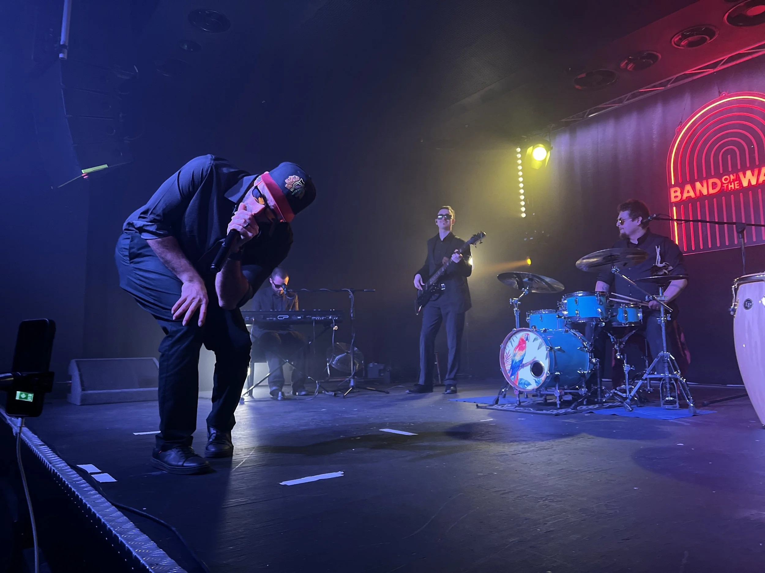 Band performing on stage at the 'Band on the Wall' venue, with one member bowing or singing into a microphone. High-end latin band in the north west of the UK, Festival Latin Band in the UK. Venezuelan Latin Band in Manchester, UK.