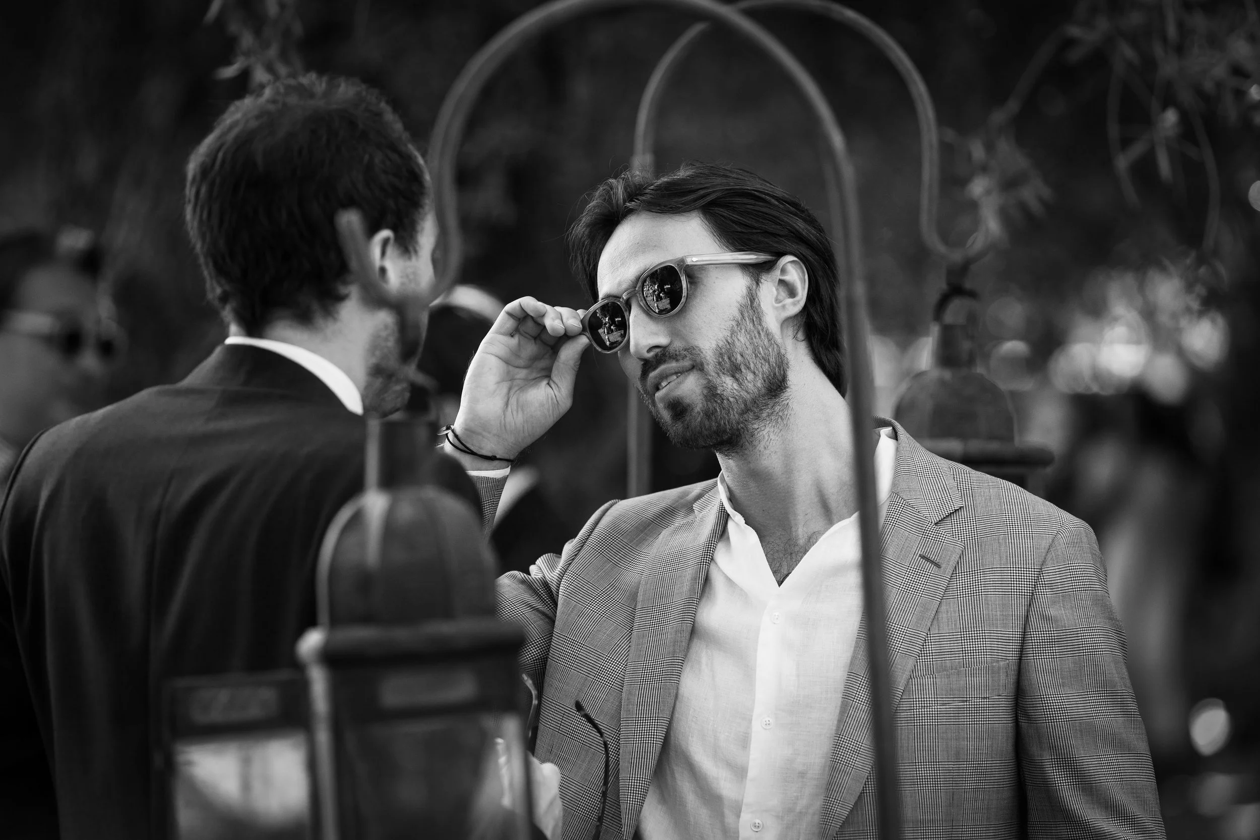 Deux hommes en costume discutent lors d'un événement en plein air, l'un d'eux portant des lunettes de soleil.