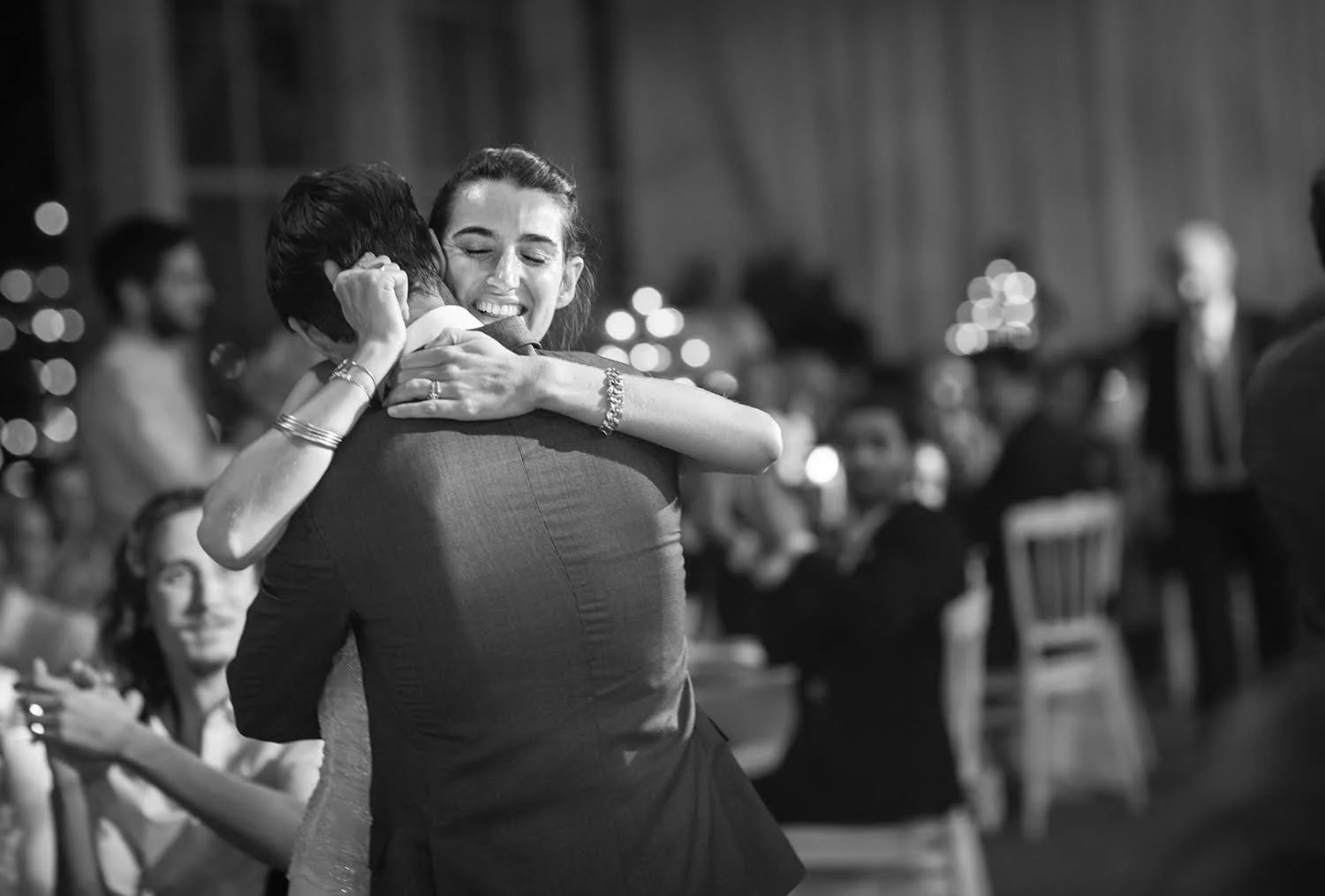 Deux personnes en costume s'étreignent lors d'une fête, en noir et blanc.