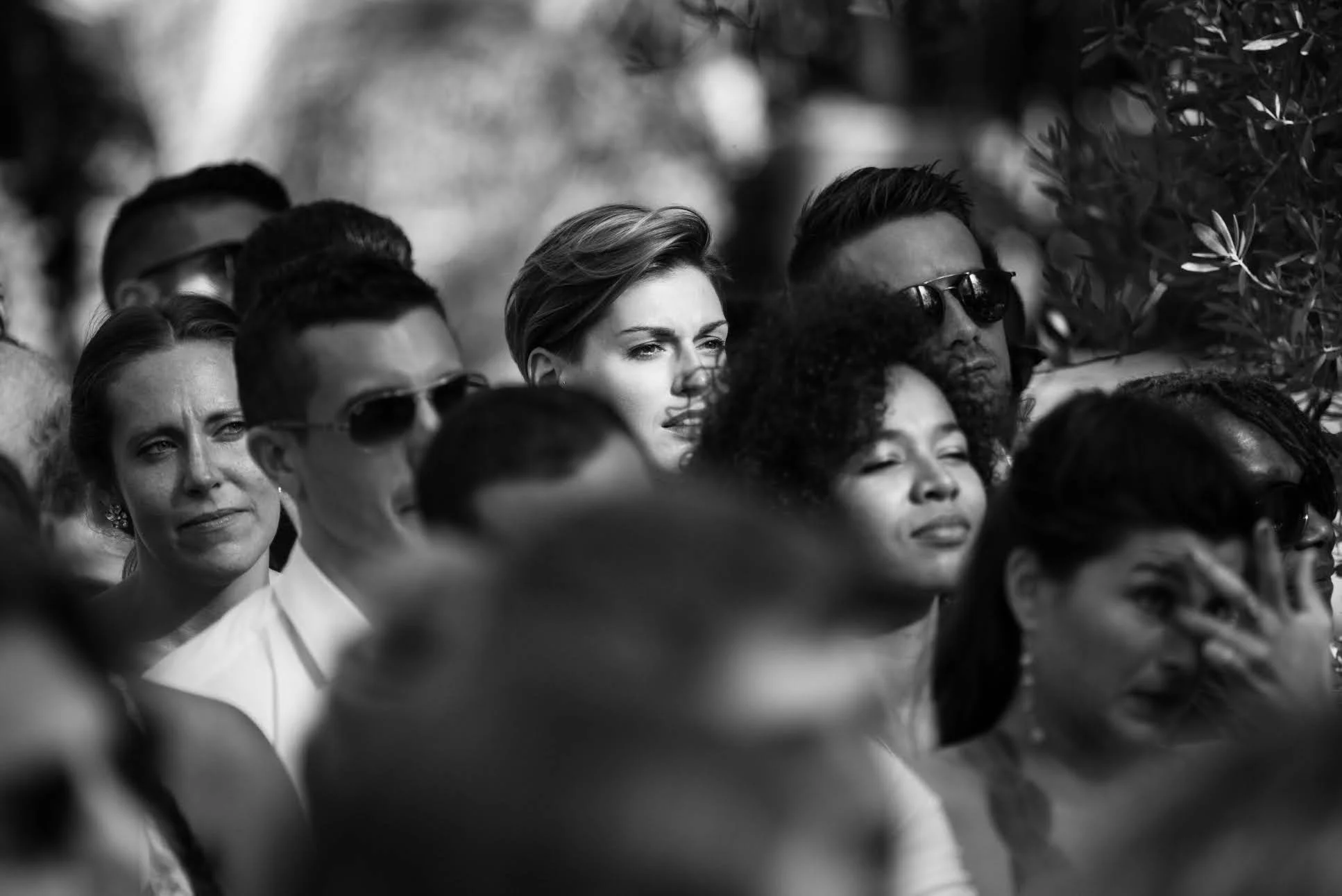Une foule de personnes regardant quelque chose à l'extérieur, certaines ont une expression émotionnelle, d'autres sont concentrées ou détendues. L'image est en noir et blanc.
