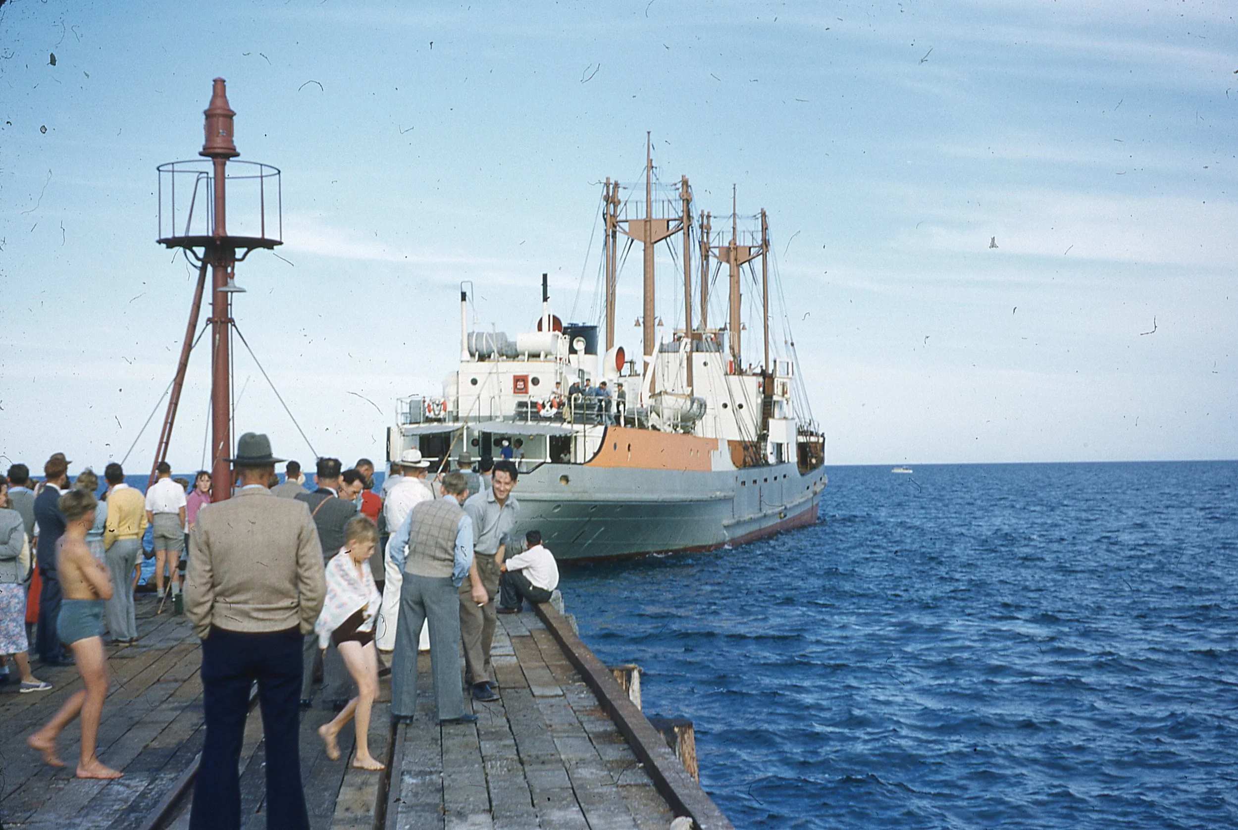 People on a dock watching a ship in the ocean during daytime.